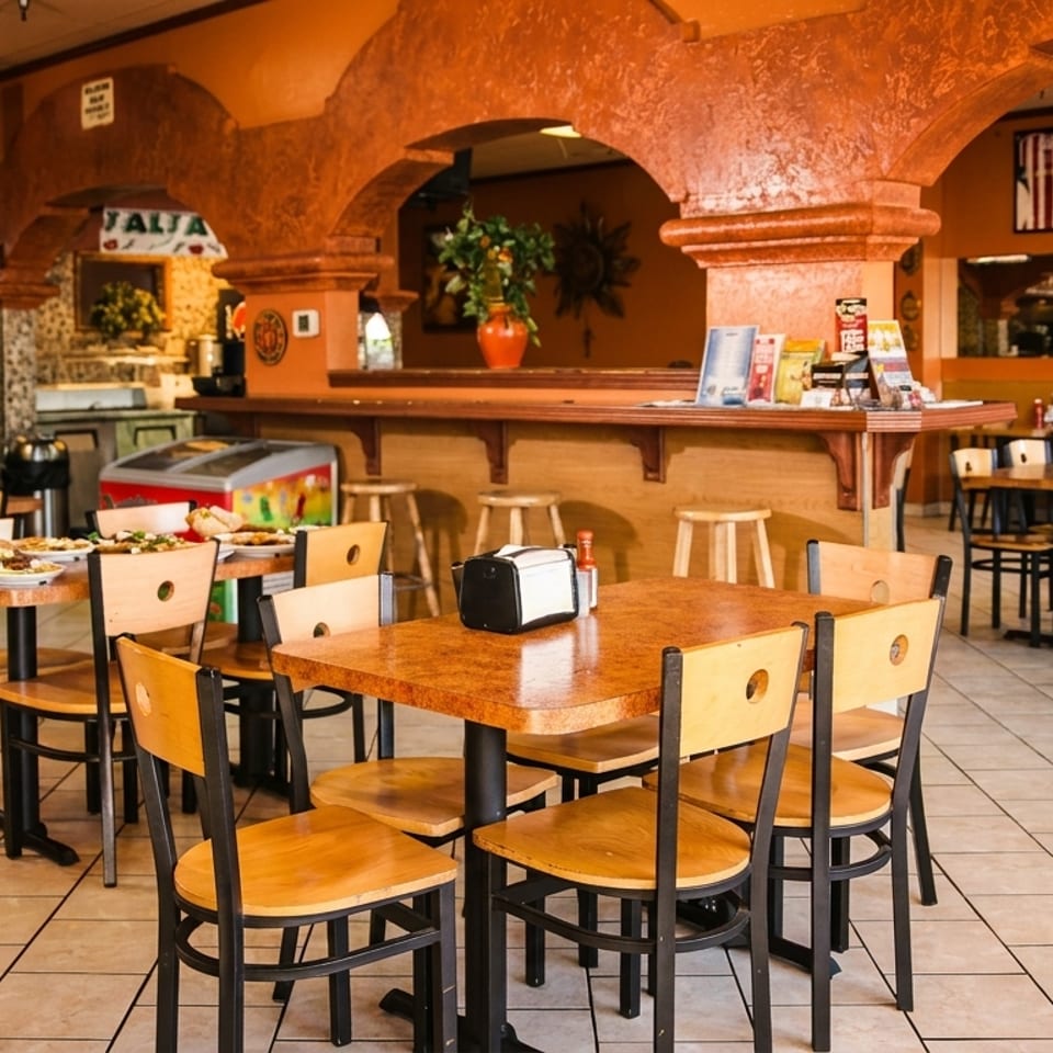Interior of a casual restaurant with orange walls, arched doorways, and empty tables with chairs.