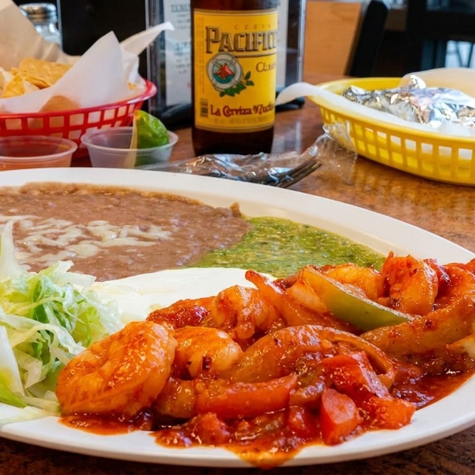 Mexican shrimp dish with refried beans, green sauce, lettuce, chips, salsa, and beer.