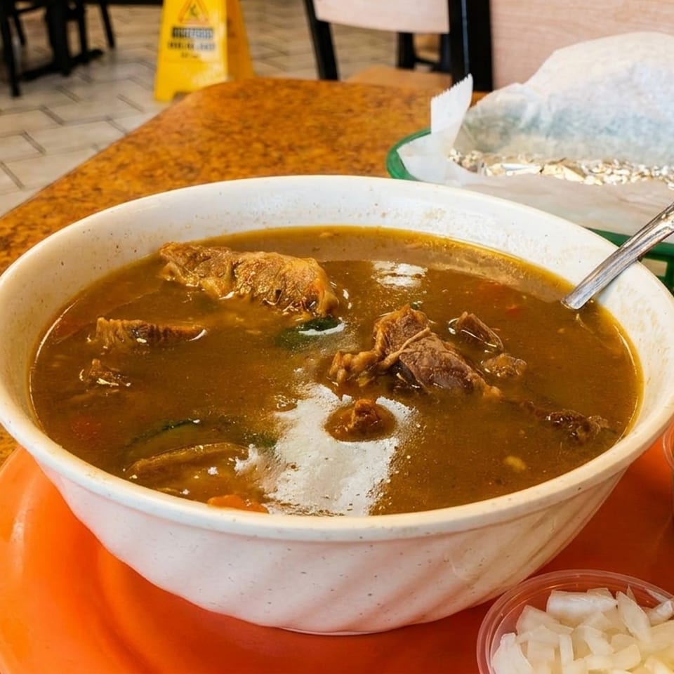 Hearty beef stew with vegetables in a white bowl, served with lime, onions, and cilantro.